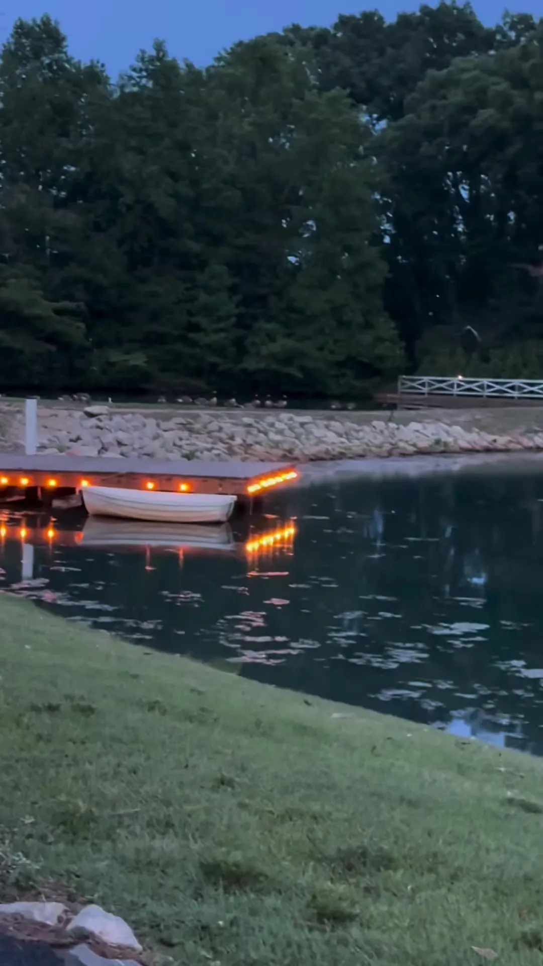 The dock lit with string lights at dusk, a rowboat tied alongside