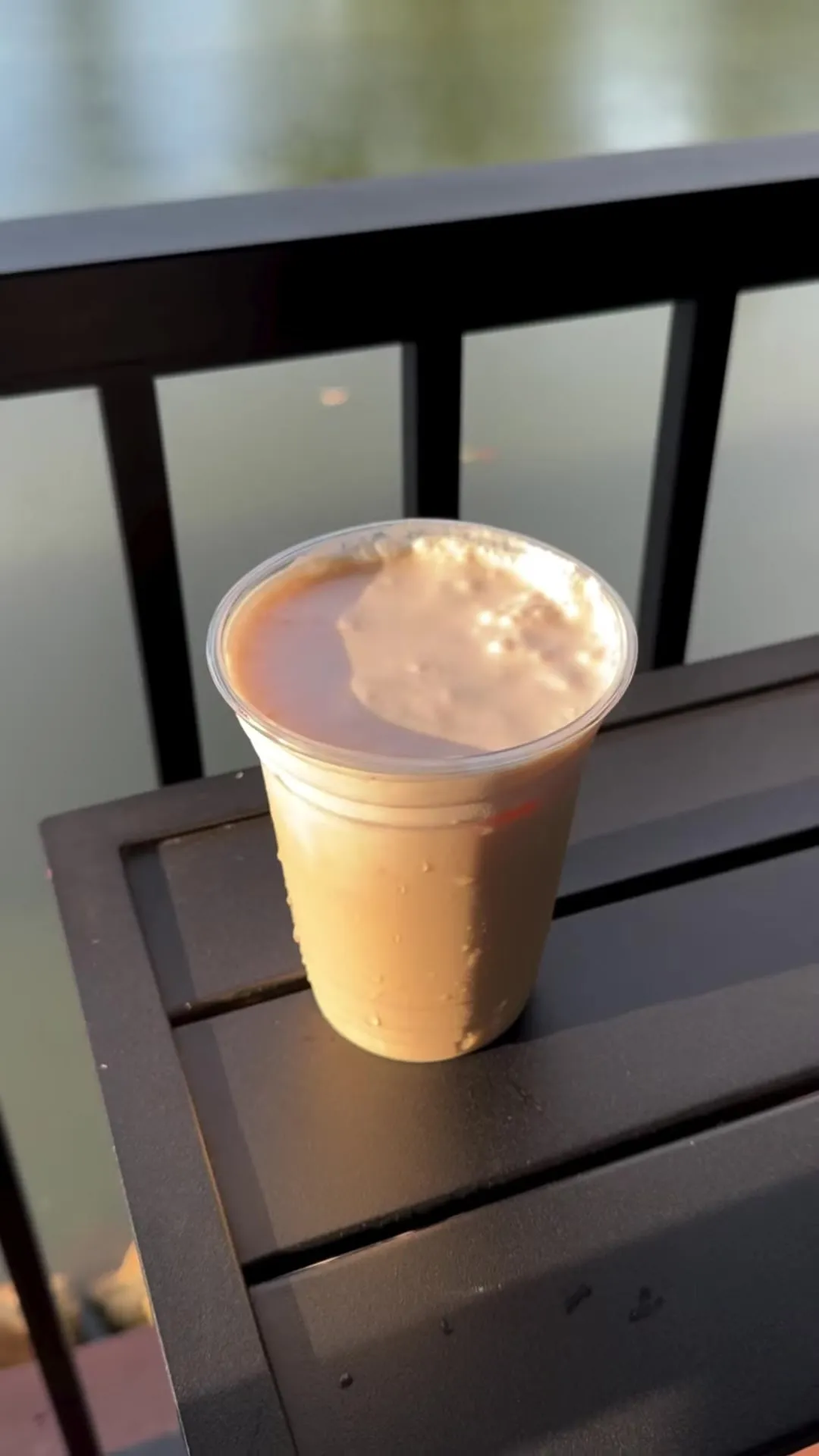 An iced latte resting on the pavilion railing above the pond